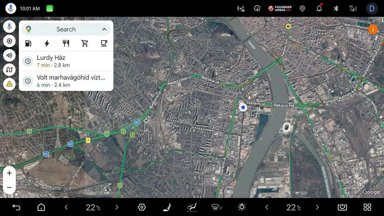 Head-unit screen showing a Google Maps satellite view of Budapest around the Danube with a search panel at the top left listing category icons (fuel, charging, food, shopping, coffee) and two recent destinations with estimated times and distances.