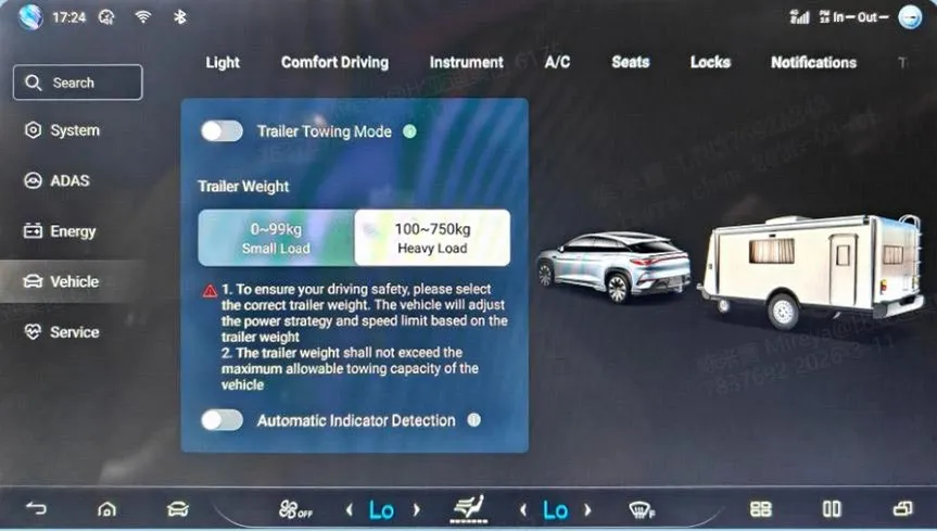 Head-unit Vehicle settings with the Trailer Towing Mode panel: a Trailer Towing Mode toggle, the weight options 099kg Small Load and 100750kg Heavy Load, safety notes about selecting the correct trailer weight and not exceeding the towing capacity, an Automatic Indicator Detection toggle, and an illustration of the car with a caravan.