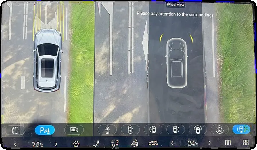 Head-unit surround-view screen showing a top-down image of the car on a narrow road beside grass verges, with the notice Please pay attention to the surroundings and the parking-view toolbar.